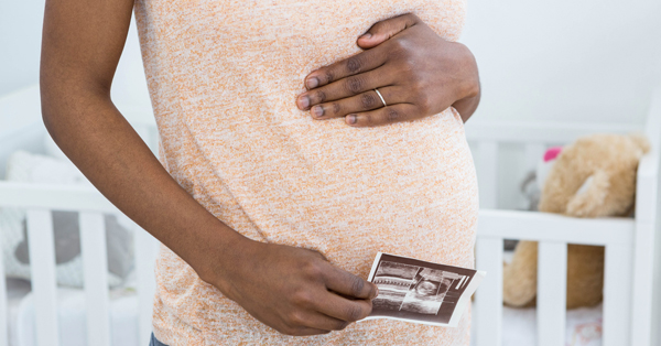 Pregnant woman’s midsection, with one hand on the top of her “bump” and the other holding a sonogram image