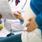 Midsection of pregnant woman pressing her hand on the side of her belly, with health care provider looking at folder in the background