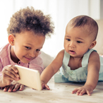 Older child showing a mobile device to a young toddler