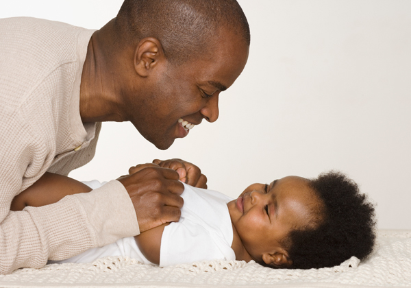 A dad smiling at a baby who is lying on her back