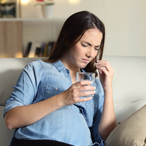 Pregnant woman with a distressed expression taking a pill.
