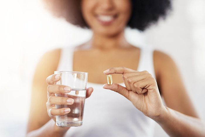 Smiling woman holding a glass of water and a pill-sized capsule.