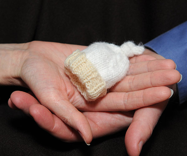 A couple’s hands holding a baby’s knitted hat.