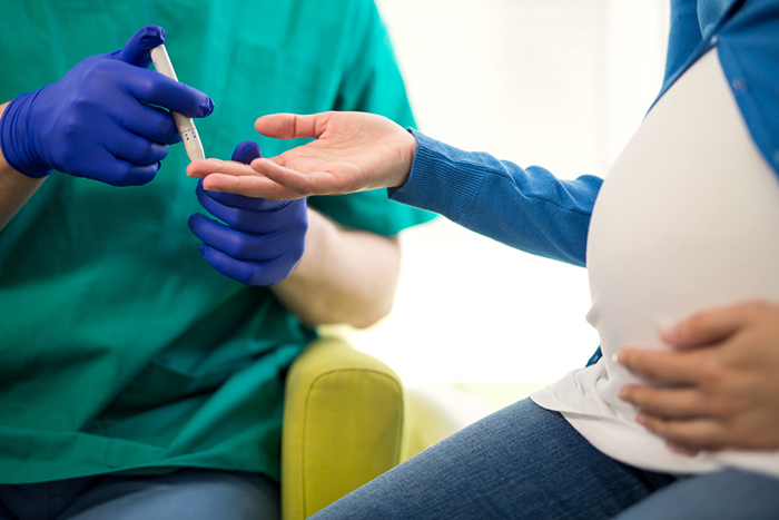 Pregnant woman offering her finger to a technician for a finger stick blood sample.