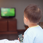 A child holding a television remote control device, facing a television set.