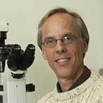 Man seated beside microscope.