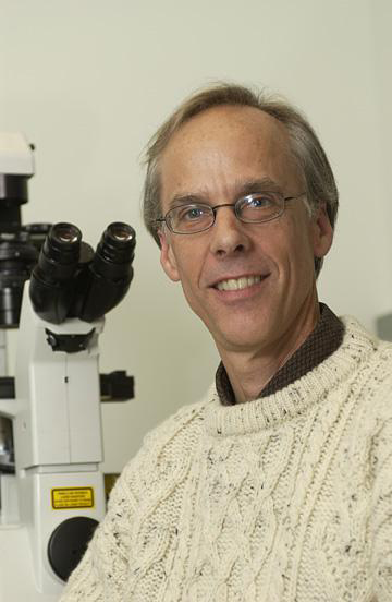 Man seated beside microscope.