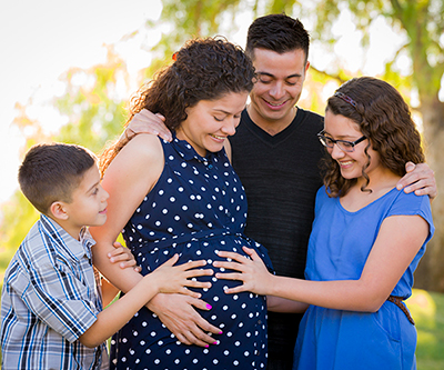 Family gathered around pregnant woman. The pregnant woman’s daughter and son are holding their hands against her stomach.