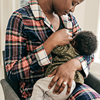 A mother breastfeeds her infant inside their home.