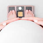 Pregnant woman stands on a scale with her hands on her belly.