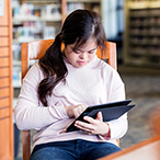 Young woman with Down syndrome typing on a computer tablet.