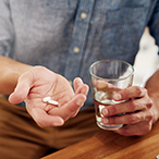 A man holds 2 pills in one hand and a glass of water in his other hand.