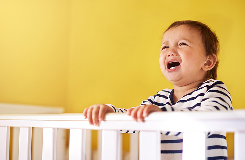 Crying toddler standing at crib rail.