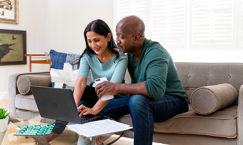 A woman and man participate in a videoconference in their living room.