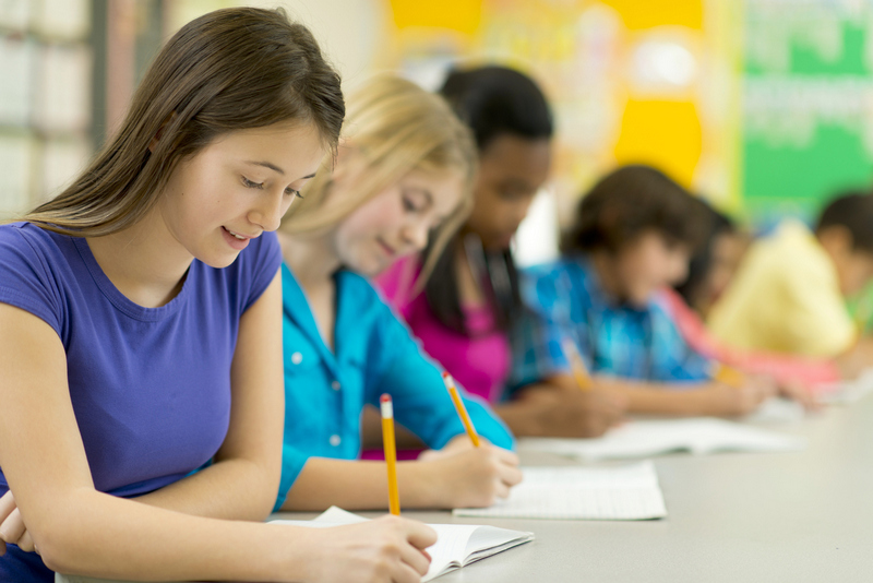 Teen boys and girls, seated at a long table, filling out a form with pencils.