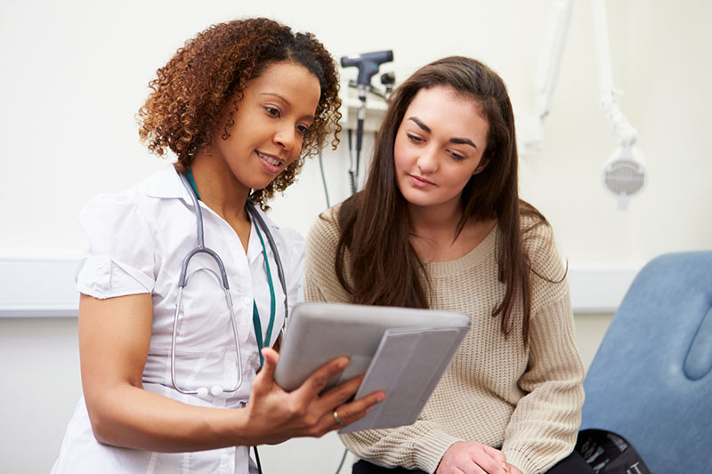 Nurse and woman looking at screen on a handheld tablet.