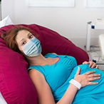 Pregnant woman with a face mask lying on an examination room table.