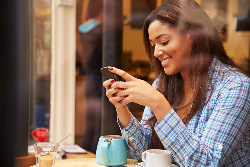 A young woman is smiling while using her cellphone.