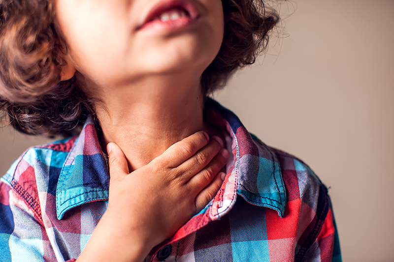 Close up of a child with their hand on their throat.