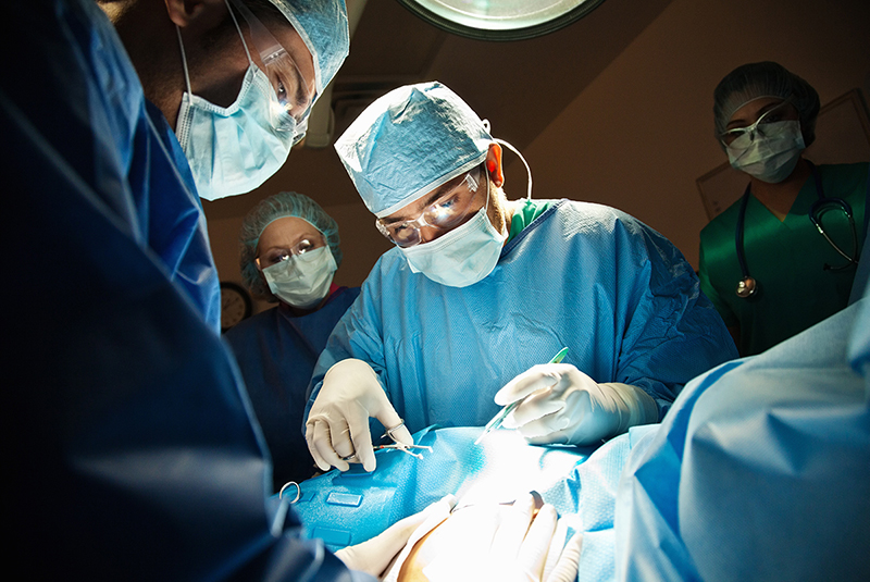 Doctors and nurses in surgical garb standing over a patient’s draped torso.