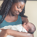 An African American woman smiling at the baby she’s holding in her arms.