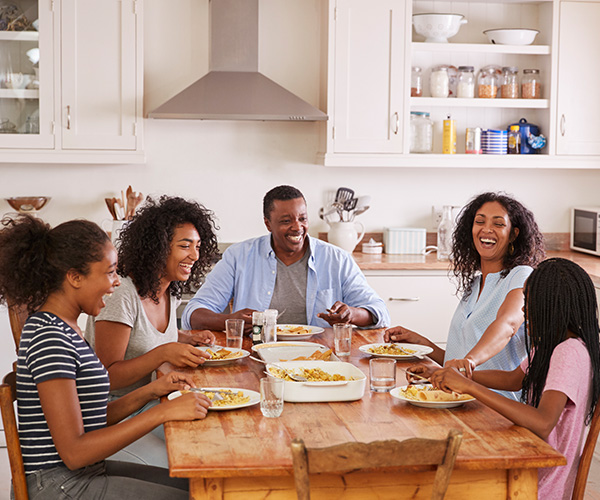 Parents and their three children sitting at their kitchen table, eating a meal together.