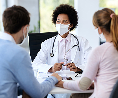 A couple holding hands as they sit and listen to a healthcare provider.