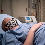 Pregnant woman wearing face mask lying in hospital bed.