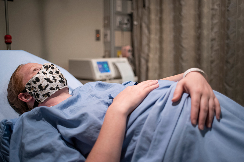 Pregnant woman wearing face mask lying in hospital bed.