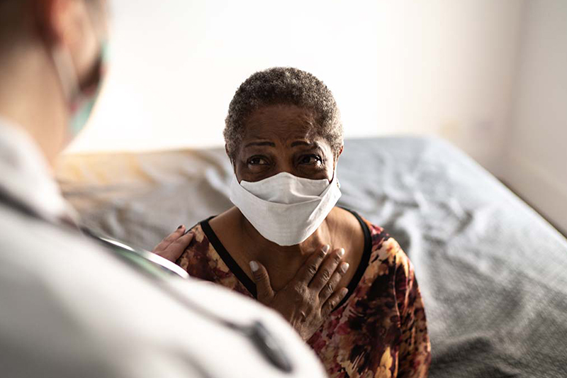 African American woman in healthcare provider’s office wearing a mask and speaking to a provider.