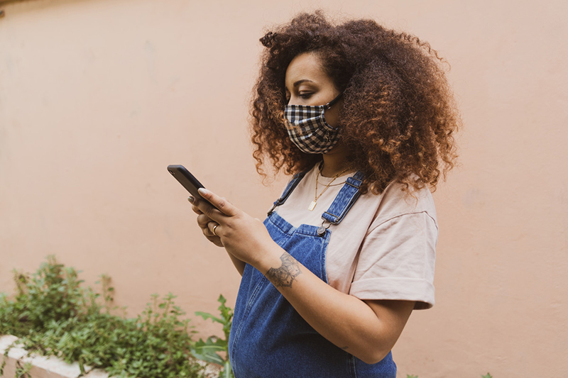 Pregnant person wearing mask checking mobile device.
