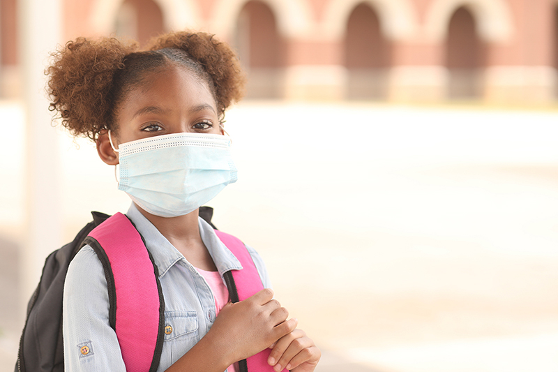 Elementary school-age Black/African American girl with backpack and wearing mask.