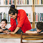 Women at long writing table with two male children