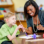 A woman and a boy with a physical disability laughing together while painting.