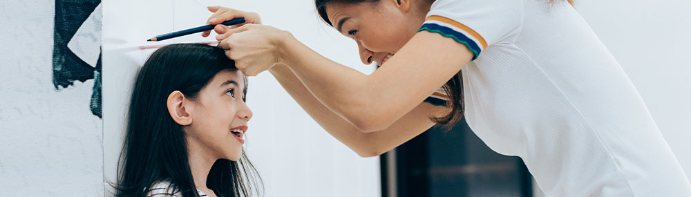 Mother measuring her child’s height with a pencil mark against a door frame.