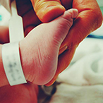 Hand holding infant foot in preparation for a heel stick.