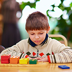 Boy seated at desk, looking down at multicolor tiles.