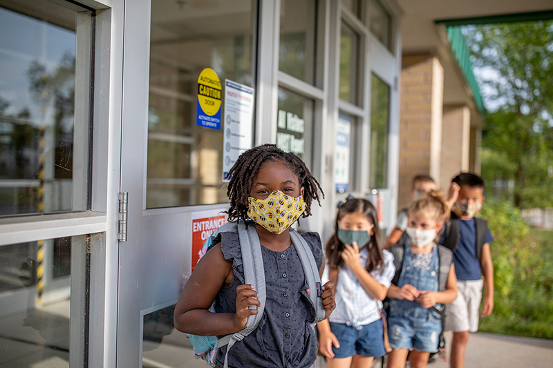 Children are lined up outside a school wearing facemasks.