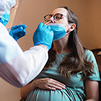 Pregnant person with lowered mask while a technician swabs a nostril.