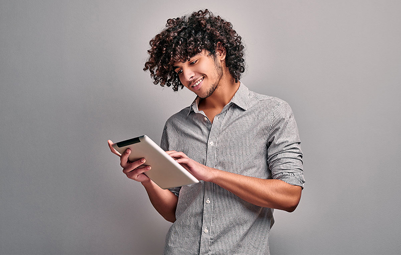 A smiling young man uses a tablet computer.