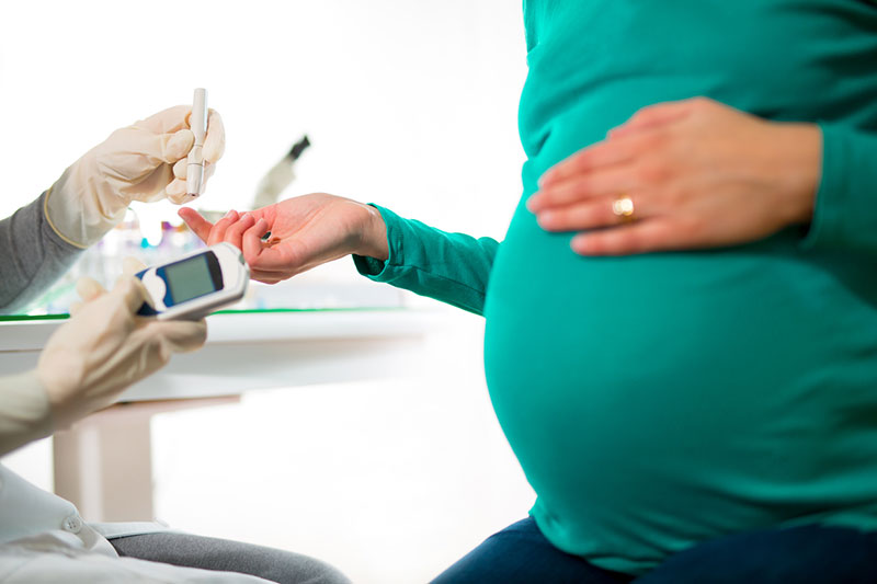 Pregnant person midsection view, holding finger out for diabetes blood test.