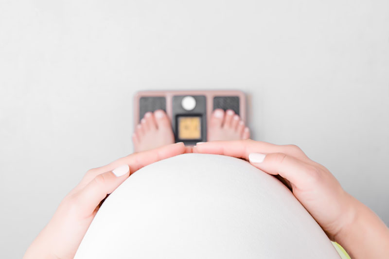 Point of view image of a pregnant person looking down at their feet on a scale.