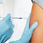 Gloved hands injecting a vaccine into a person’s arm.