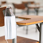 Surgical mask hanging from the seat of a classroom desk.