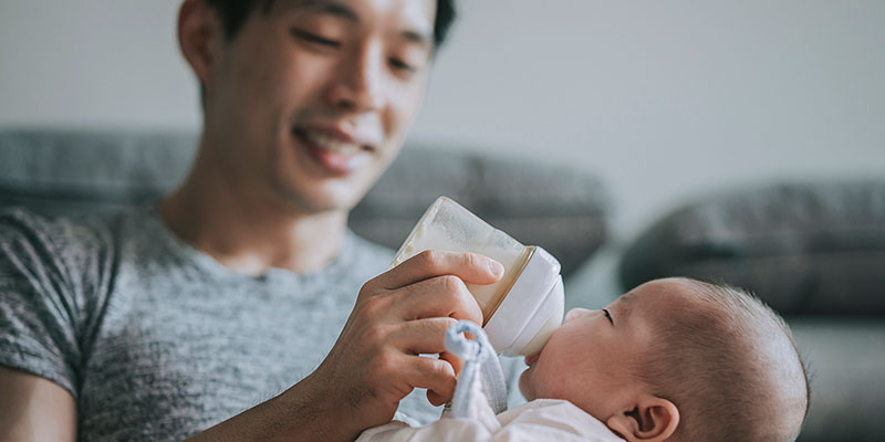 A man bottle-feeding a baby.