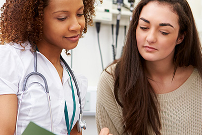 A healthcare provider and a patient reading a medical booklet together in an examining room.