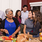 Multi-ethnic, multi-generational family members prepare a holiday dinner together in their home kitchen.