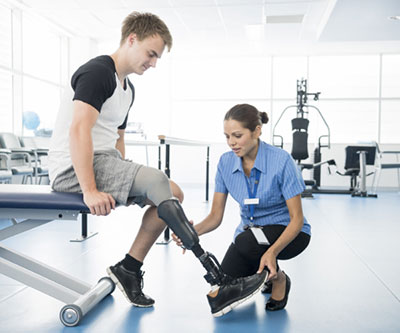 A healthcare provider, who is crouched on the ground, adjusts a man’s prosthetic leg.