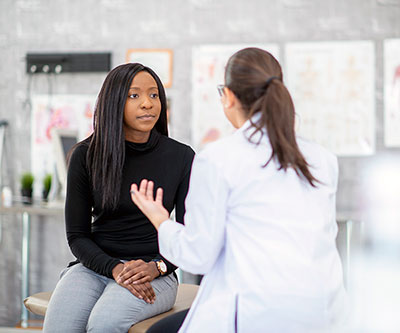 A healthcare provider, who has her back turned to the camera, speaks with a patient who is facing the camera.