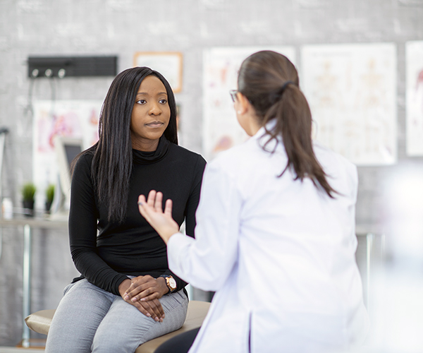 A healthcare provider, who has her back turned to the camera, speaks with a patient who is facing the camera.